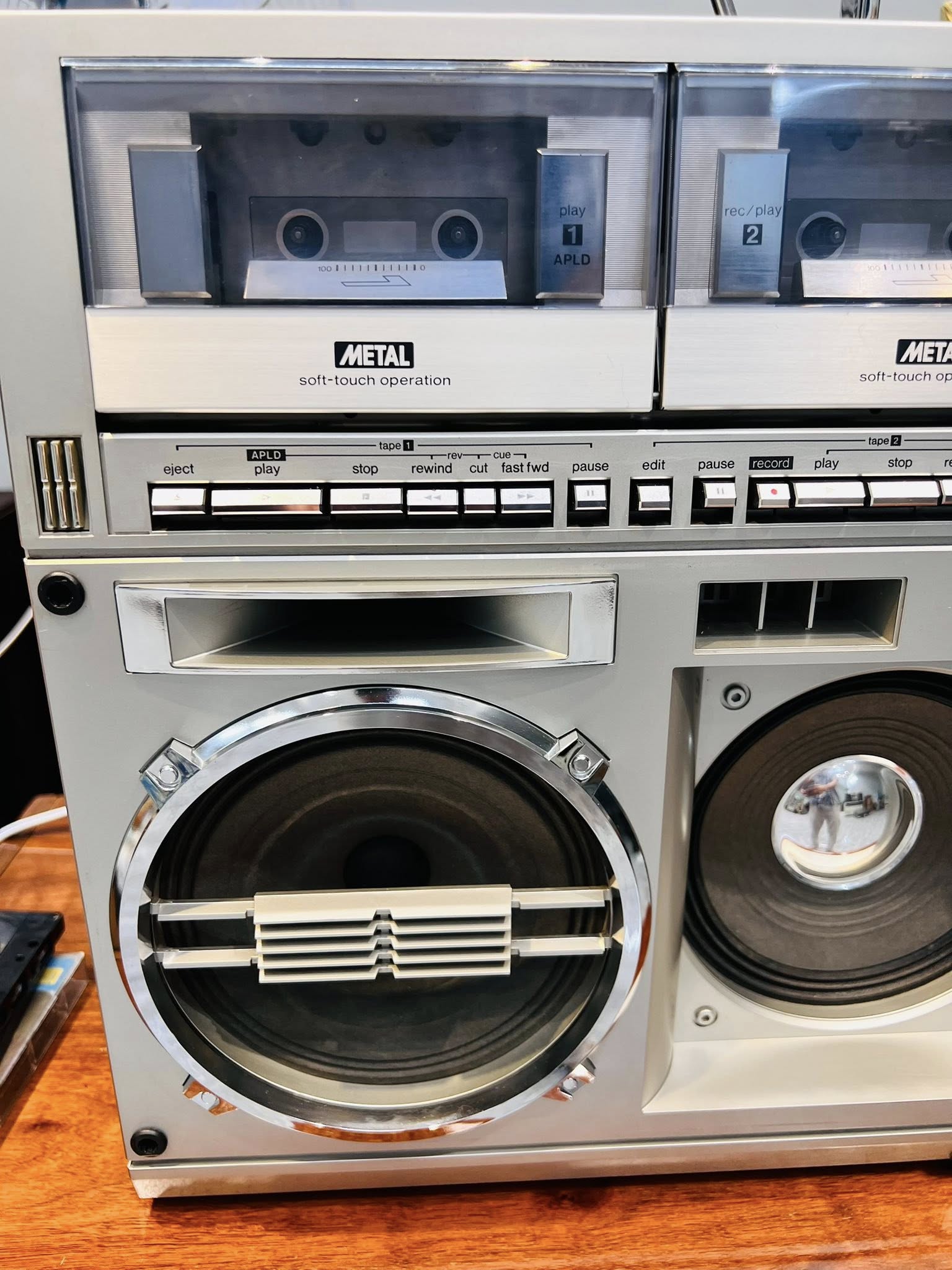 Dàn cassette boombox cổ điển màu bạc với hai deck băng và loa lớn trên mặt gỗ