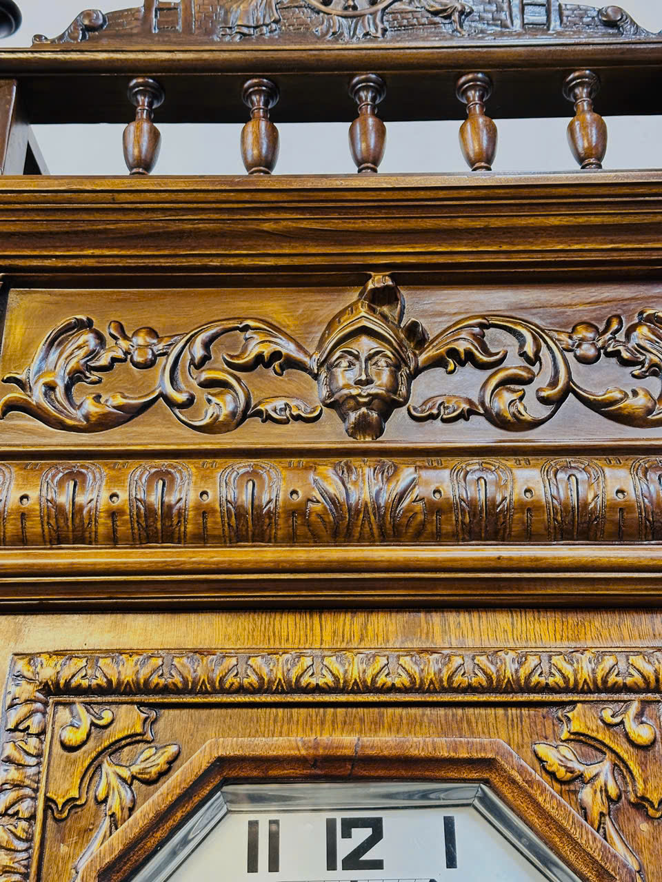 Chi tiết chạm khắc gỗ trên thân đồng hồ treo tường cổ điển với hoa văn và khuôn mặt người